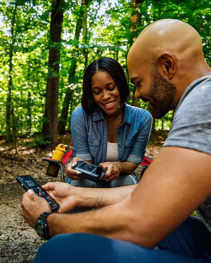Two campers using a portable satellite hotspot in woodland