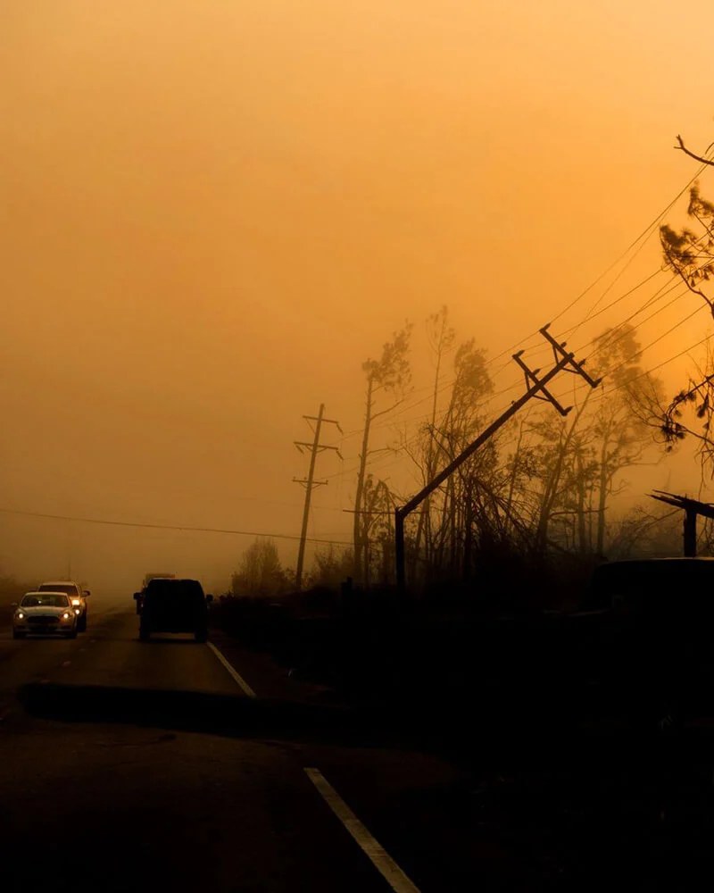 Vehicles evacuating along a smoke-filled road at dusk